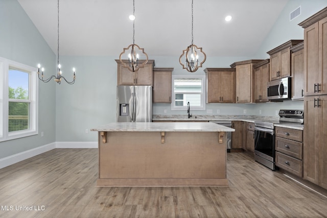 kitchen with a center island, stainless steel appliances, decorative light fixtures, and light hardwood / wood-style flooring