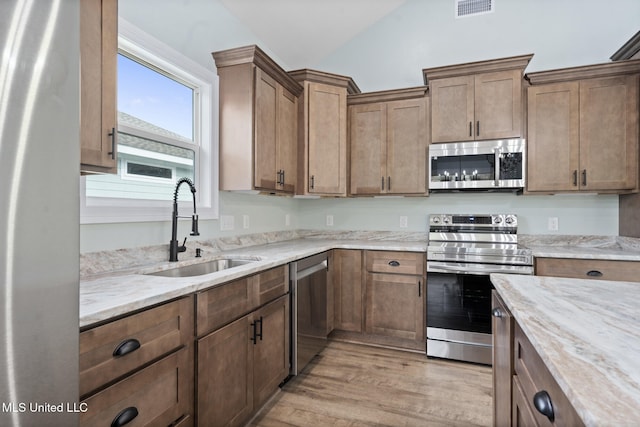 kitchen with sink, vaulted ceiling, light stone countertops, appliances with stainless steel finishes, and light hardwood / wood-style floors