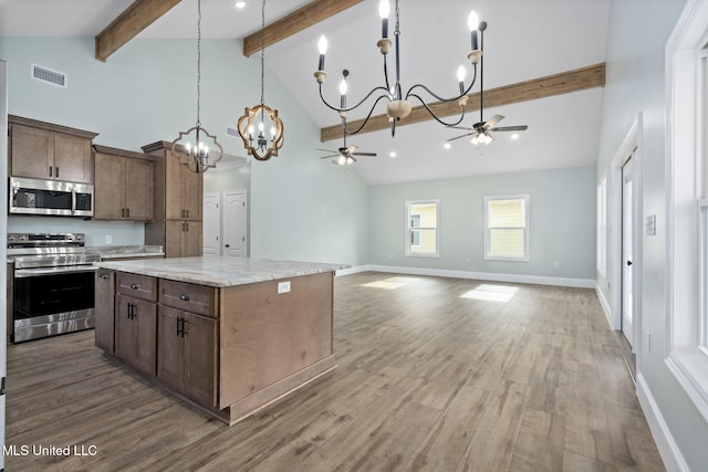 kitchen with hardwood / wood-style floors, high vaulted ceiling, ceiling fan with notable chandelier, appliances with stainless steel finishes, and a kitchen island