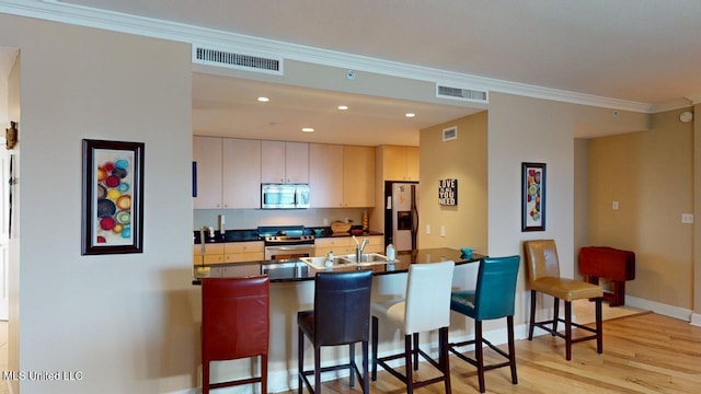 kitchen featuring stainless steel appliances, ornamental molding, sink, and light hardwood / wood-style flooring