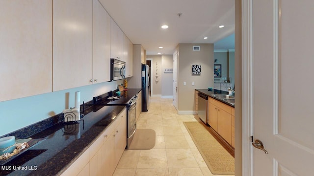 kitchen with appliances with stainless steel finishes, sink, white cabinets, dark stone counters, and light tile patterned floors