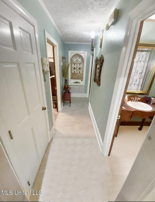 corridor with sink, crown molding, light carpet, and a textured ceiling