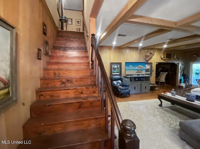 staircase featuring wood walls and beamed ceiling