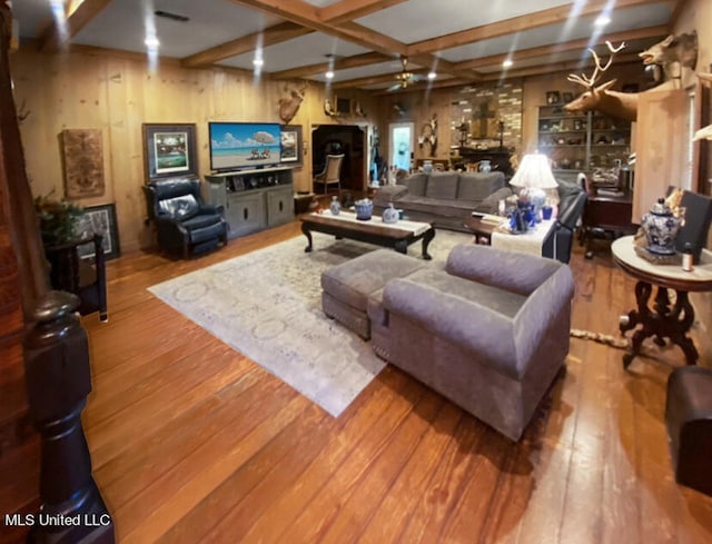 living room featuring wood walls, hardwood / wood-style floors, beamed ceiling, and ceiling fan