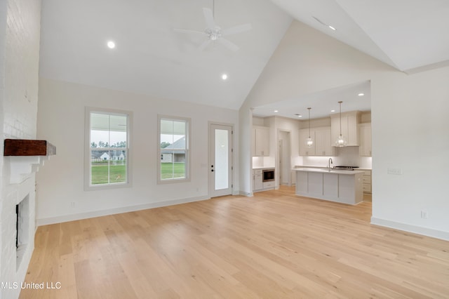 unfurnished living room with sink, light hardwood / wood-style floors, high vaulted ceiling, and ceiling fan