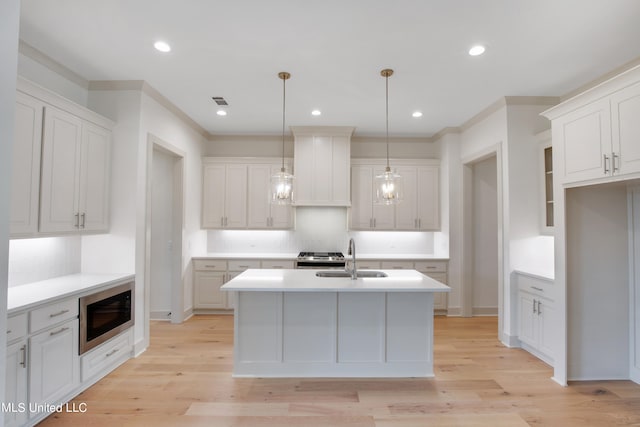 kitchen featuring sink, stainless steel microwave, white cabinetry, decorative light fixtures, and a center island with sink