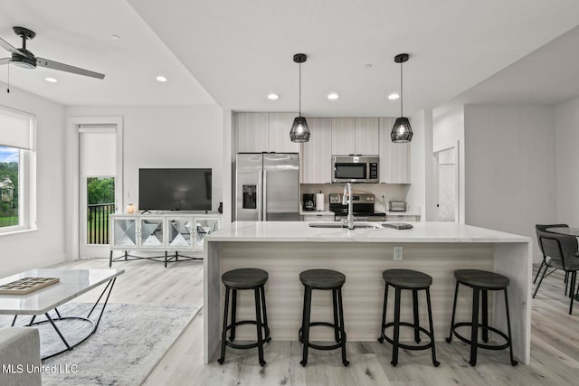 kitchen featuring appliances with stainless steel finishes, a kitchen island with sink, light wood-type flooring, sink, and decorative light fixtures