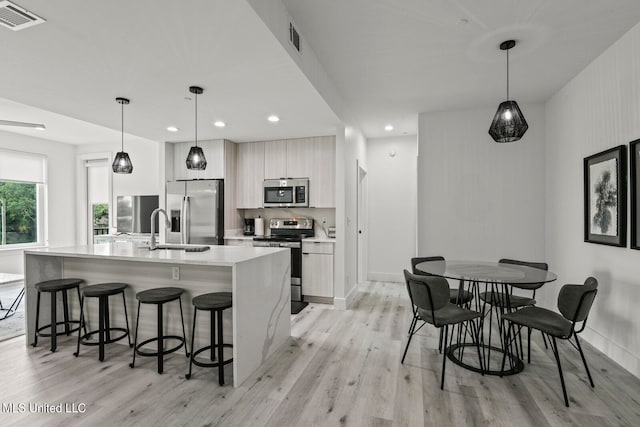 kitchen featuring light hardwood / wood-style flooring, a center island with sink, sink, decorative light fixtures, and appliances with stainless steel finishes