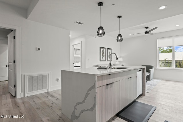 kitchen featuring sink, hanging light fixtures, ceiling fan, light hardwood / wood-style flooring, and a kitchen island with sink