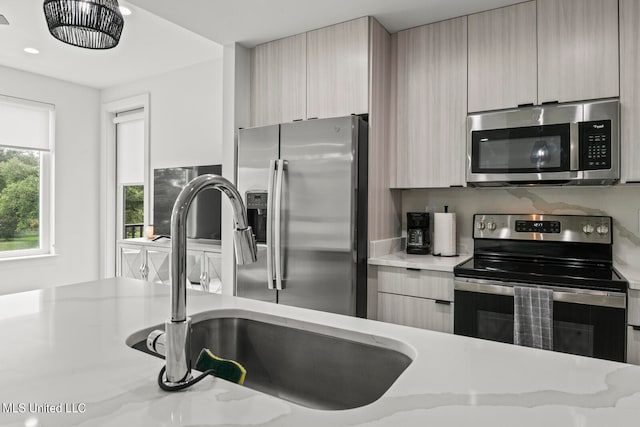 kitchen featuring appliances with stainless steel finishes, light stone countertops, sink, and light brown cabinetry