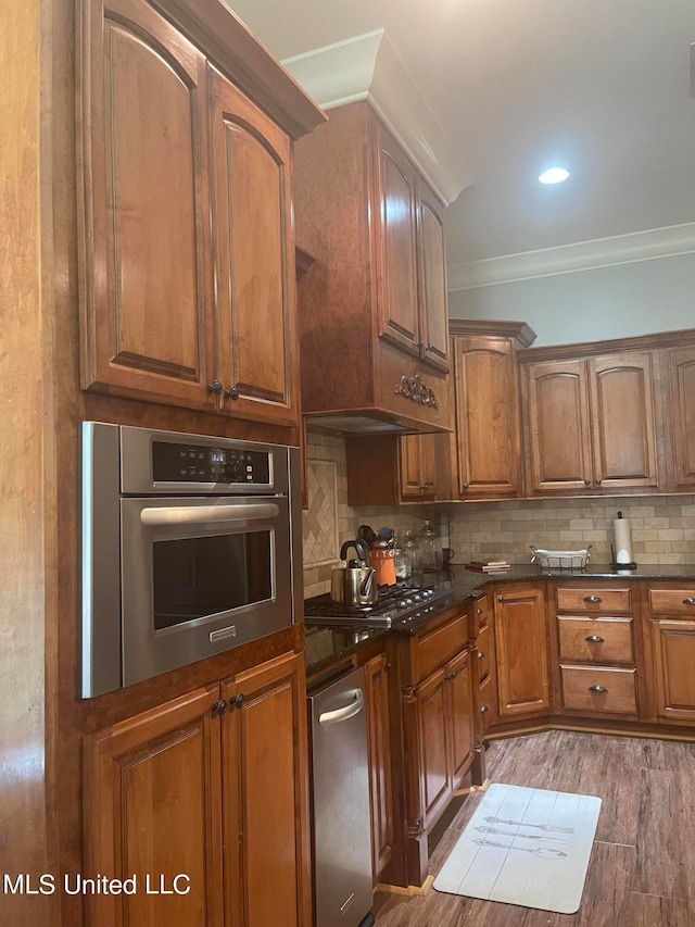 kitchen featuring backsplash, stainless steel appliances, wood-type flooring, and ornamental molding