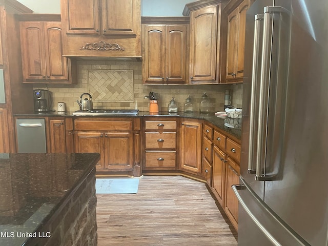 kitchen featuring appliances with stainless steel finishes, light hardwood / wood-style flooring, dark stone counters, and backsplash