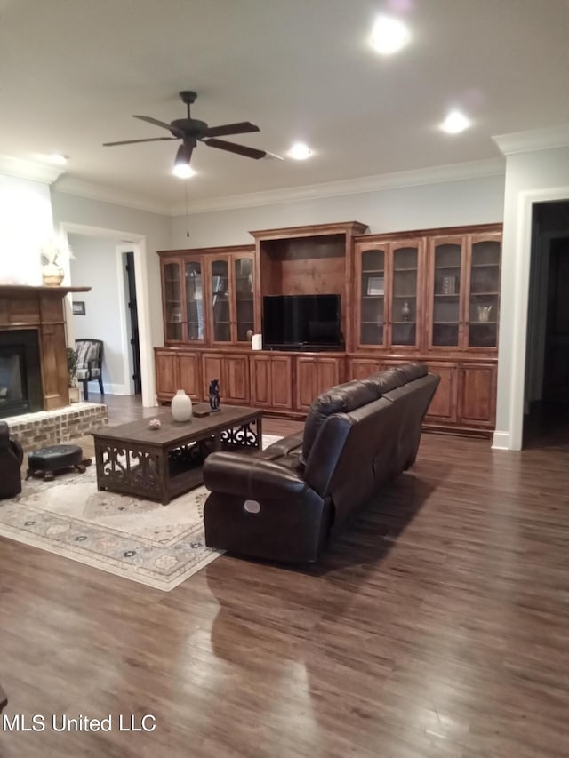 living room featuring crown molding, a brick fireplace, dark hardwood / wood-style floors, and ceiling fan