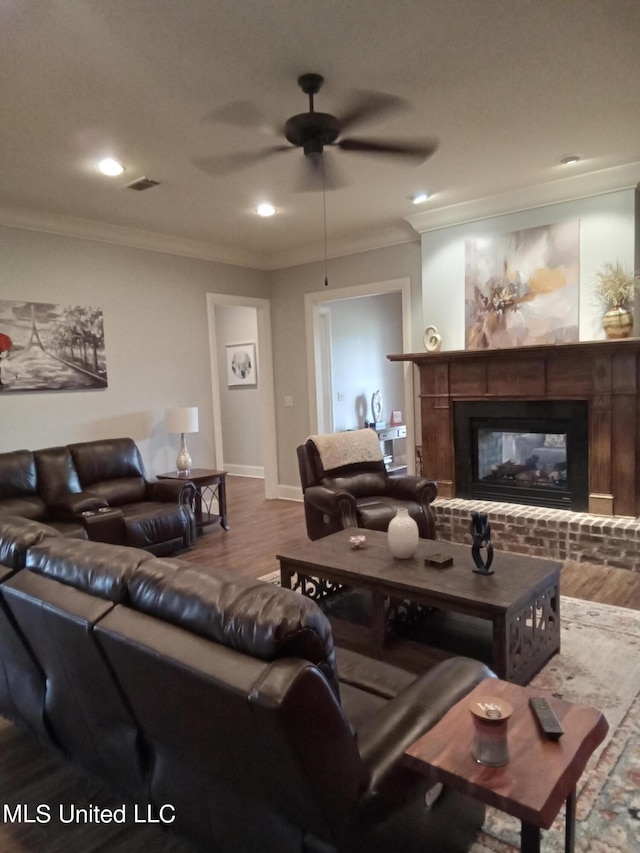 living room featuring crown molding, ceiling fan, wood-type flooring, and a brick fireplace