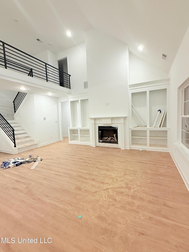 unfurnished living room featuring light wood-type flooring, high vaulted ceiling, and built in features