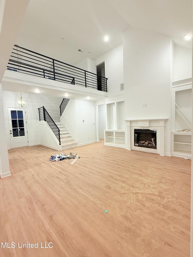 unfurnished living room featuring built in features, high vaulted ceiling, an inviting chandelier, and light hardwood / wood-style flooring