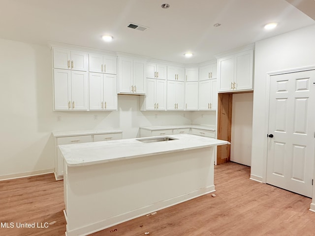 kitchen with light wood-type flooring, a center island with sink, and white cabinets