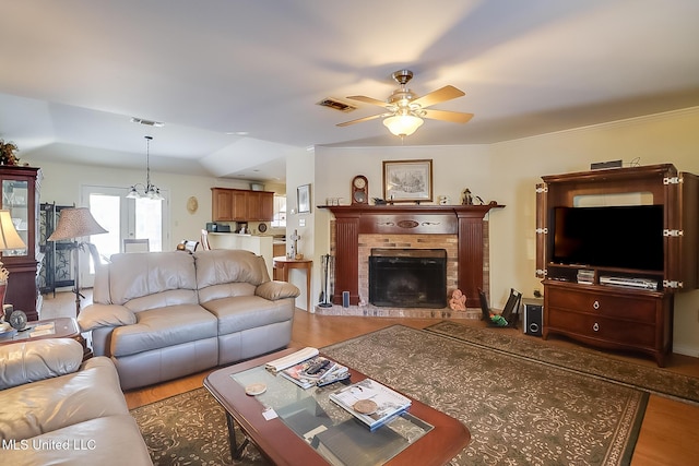 living room with ceiling fan with notable chandelier, a brick fireplace, and light wood-type flooring