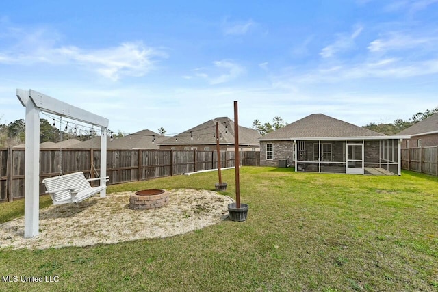 view of yard featuring a sunroom, a fenced backyard, and an outdoor fire pit