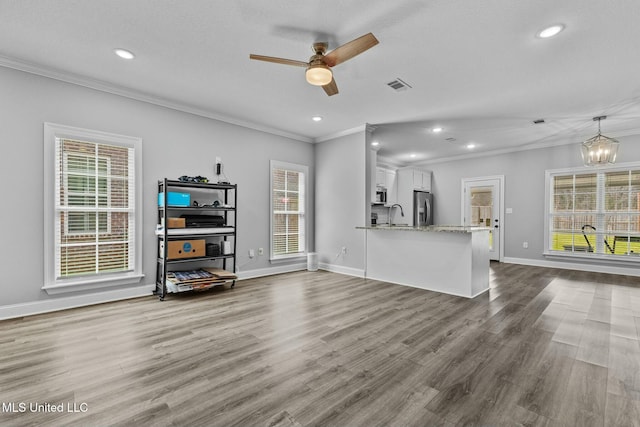 unfurnished living room with visible vents, ceiling fan with notable chandelier, a sink, crown molding, and dark wood-style flooring