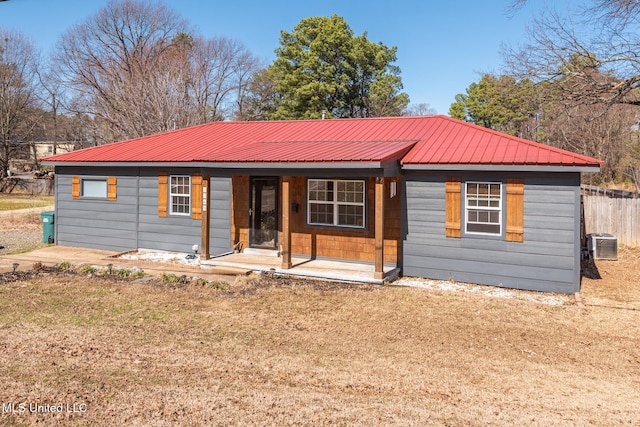 view of front of property featuring metal roof, fence, a front lawn, and central air condition unit