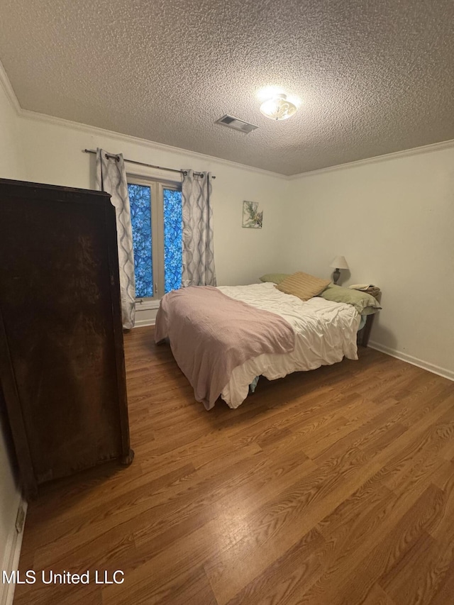 bedroom with a textured ceiling, wood finished floors, and crown molding
