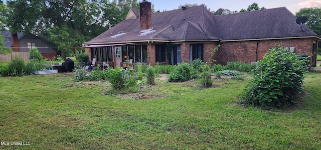 rear view of house featuring a yard, a chimney, and brick siding