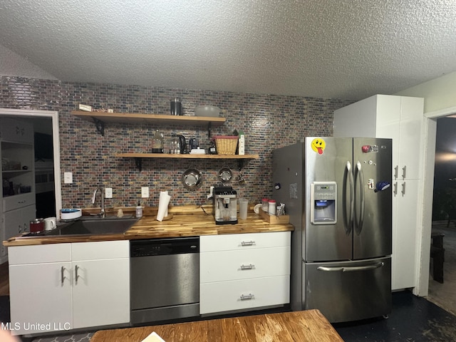 kitchen featuring appliances with stainless steel finishes, butcher block counters, a textured ceiling, a sink, and white cabinets