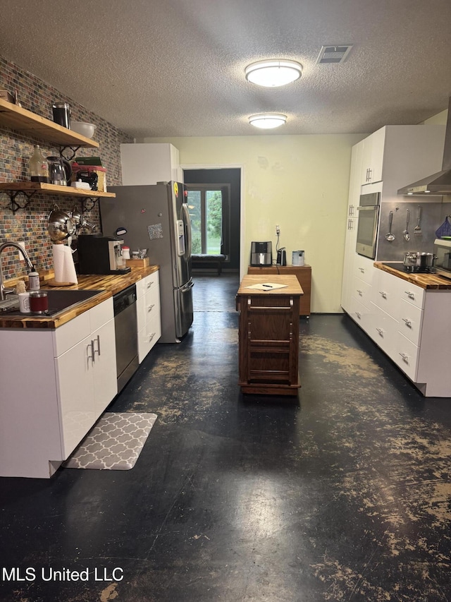 kitchen featuring appliances with stainless steel finishes, a sink, white cabinets, open shelves, and wall chimney range hood