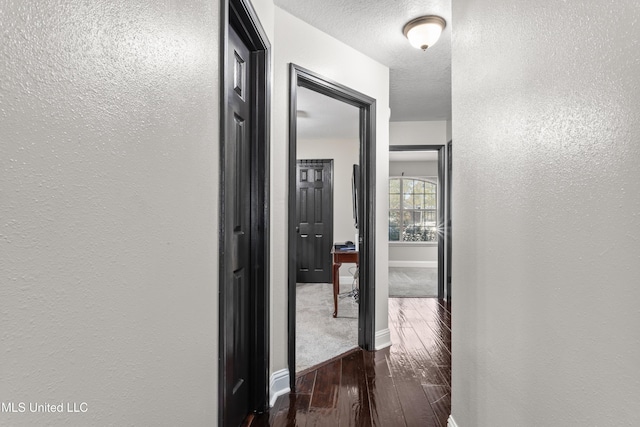 hallway with a textured ceiling and dark hardwood / wood-style floors