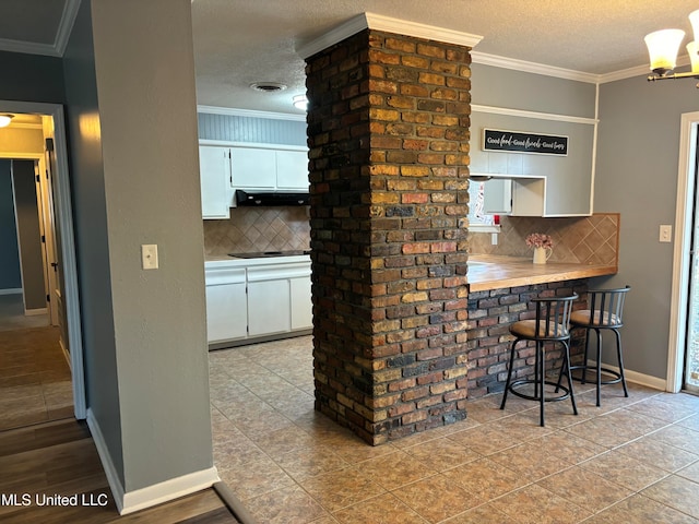 kitchen featuring tasteful backsplash, white cabinetry, a kitchen bar, and ornamental molding