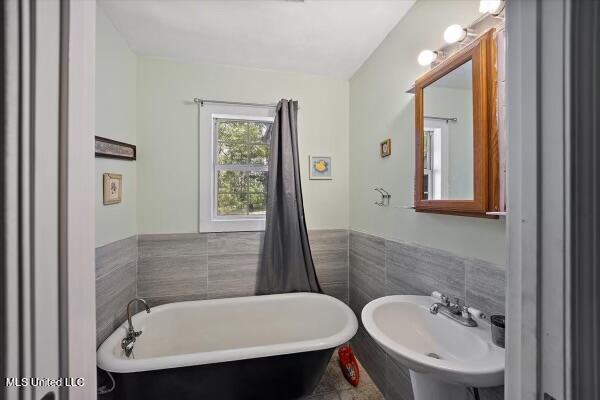 bathroom with tile walls, sink, and a tub to relax in