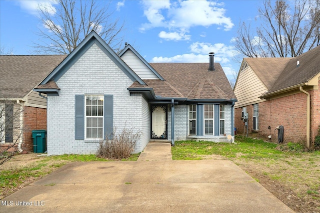 view of front of home featuring a shingled roof, a front yard, and brick siding