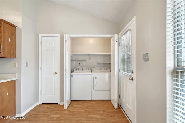 clothes washing area with laundry area, washing machine and dryer, light wood finished floors, and a wealth of natural light