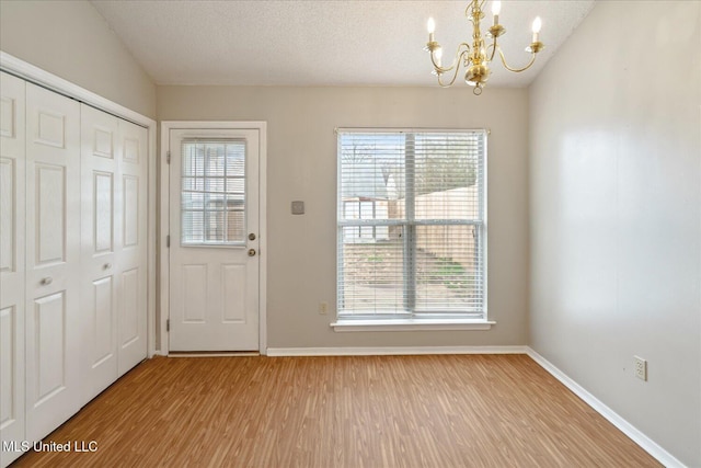 doorway with a healthy amount of sunlight, a notable chandelier, a textured ceiling, and wood finished floors