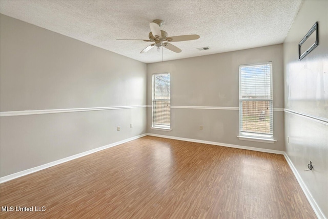 empty room with visible vents, a ceiling fan, a textured ceiling, wood finished floors, and baseboards