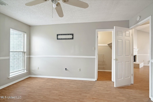 unfurnished bedroom featuring a textured ceiling, a spacious closet, light wood finished floors, and visible vents