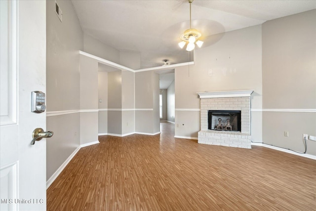 unfurnished living room featuring baseboards, visible vents, ceiling fan, wood finished floors, and a fireplace