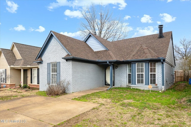 view of front of property with a shingled roof, a front yard, brick siding, and fence