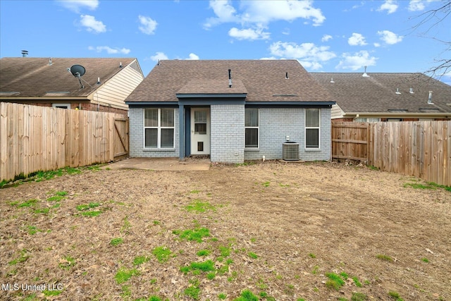 rear view of property featuring a fenced backyard, a shingled roof, central AC, and brick siding