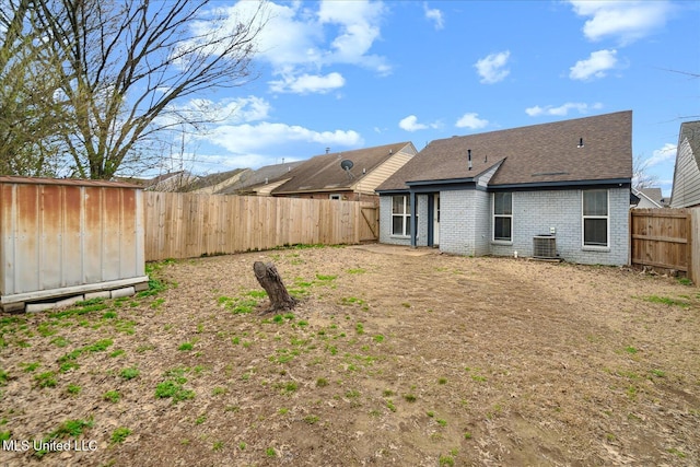 back of house with brick siding, roof with shingles, central AC, a fenced backyard, and an outdoor structure