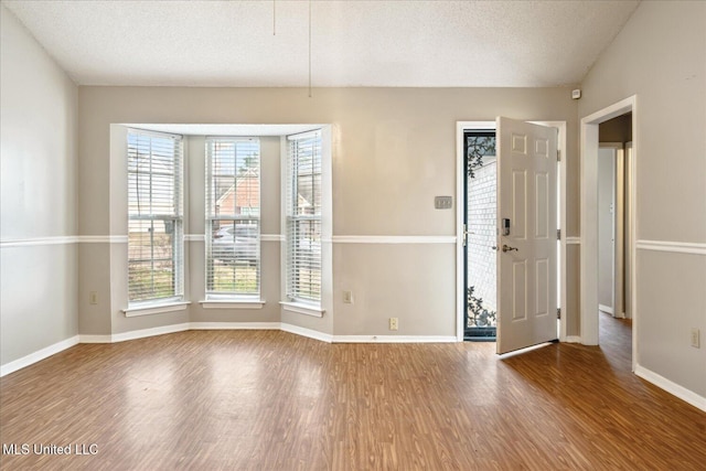 spare room featuring a textured ceiling, baseboards, and wood finished floors