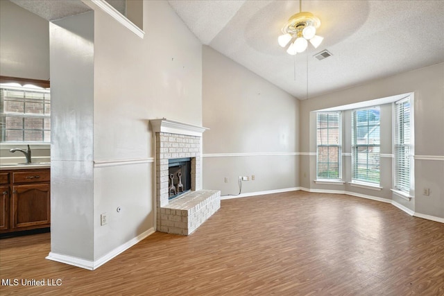 unfurnished living room with visible vents, lofted ceiling, wood finished floors, a fireplace, and a sink