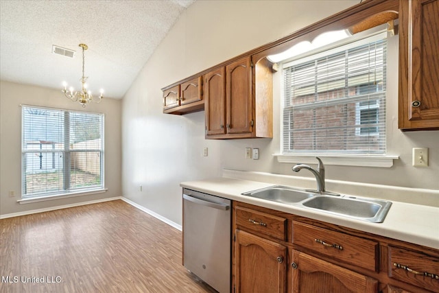 kitchen with visible vents, brown cabinets, vaulted ceiling, stainless steel dishwasher, and a sink