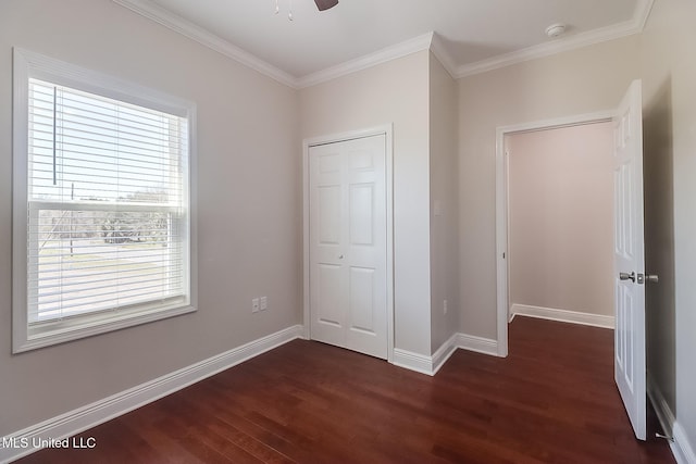 unfurnished bedroom featuring crown molding, a closet, dark wood finished floors, and baseboards