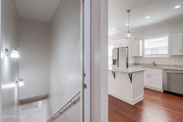 kitchen featuring pendant lighting, appliances with stainless steel finishes, white cabinets, a sink, and light stone countertops