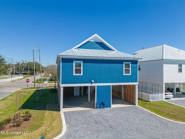 view of front of property with gravel driveway, a front lawn, metal roof, and a carport