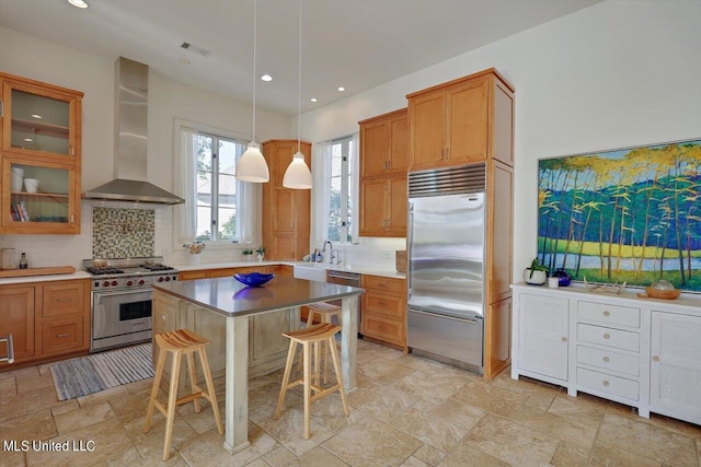 kitchen featuring decorative backsplash, wall chimney exhaust hood, a breakfast bar area, high quality appliances, and decorative light fixtures