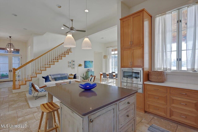 kitchen featuring backsplash, ceiling fan, stainless steel microwave, a center island, and decorative light fixtures