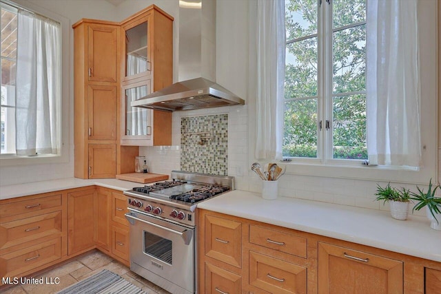 kitchen with wall chimney exhaust hood, tasteful backsplash, and premium stove